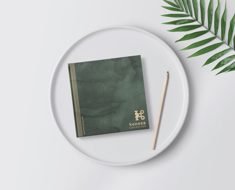 Cuadernillo cuadrado y un lápiz juto a una planta