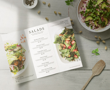 Раскрытое меню-буклет рядом с тарелкой салата